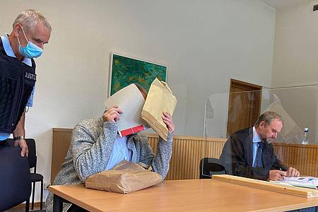 Der Angeklagte im sogenannten Cophunter-Prozess sitzt im Gerichtssaal des Amtsgerichts Idar-Oberstein und hält sich Akten vor sein Gesicht.
