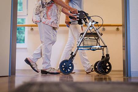 Eine Pflegekraft geht in einem Stuttgarter Pflegeheim mit einer älteren Frau über den Flur.