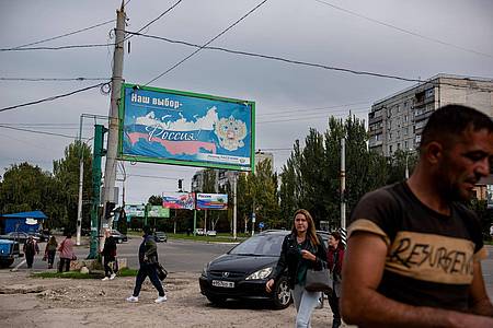 Menschen gehen in der von Russland unterstützten und von Separatisten kontrollierten Volksrepublik Luhansk in der Ostukraine an einem Plakat mit der Aufschrift «Unsere Wahl - Russland» vorbei.