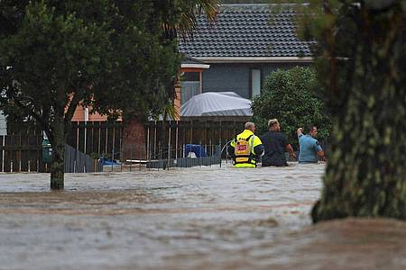 Menschen waten durch das Hochwasser einer vollkommen überschwemmten Straße in Auckland.
