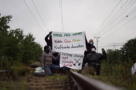 Klimaaktivisten der Gruppe "unfreiwillige Feuerwehr" blockieren Gleise am Kohlekraftwerk Jänschwalde und posieren mit Plakaten "Fossil free future".