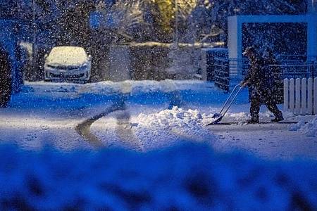 Ein Mann räumt am frühen Morgen Schnee auf einer Straße.