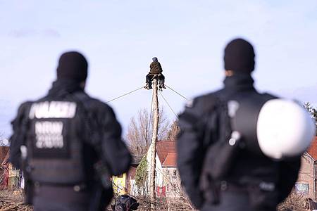 Polizisten beobachten zwei Klimaschutzaktivisten die auf einem Monopod am Rand des Braunkohledorfes Lützerath sitzen.