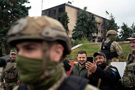 Der ukrainische Präsident Wolodymyr Selenskyj (M) macht in Isjum ein Selfie mit einem Polizisten.