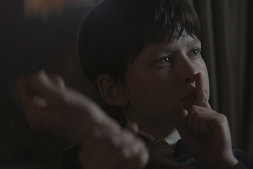 Ein Junge hält einen Finger vor seine Lippen