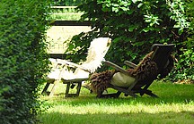 Hölzerne Liegestühle mit Fellen in sonnig, grünem Garten